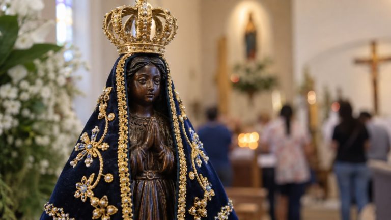 Imagem de Nossa Senhora Aparecida com manto azul e coroa em ambiente de igreja